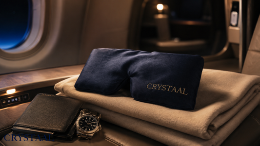 Masque de nuit en pure soie de mûrier Crystaal avec bandeau large enveloppant posé sur une couverture en cachemire dans une cabine business class lors d'un vol long-courrier, illustrant l'équipement anti jet-lag pour entrepreneurs et digital nomads.